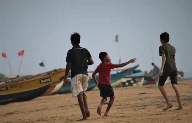 Three children playing on the beach in Sri Lanka, with fishing boats in the background